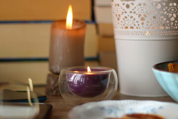 Notebook, pen, tablet, reading glasses, books, phone, candle, bowl of biscuits and cup of tea on the table. Selective focus.