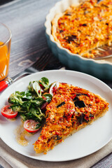 Quiche with carrots, peppers and eggplant, served on a plate with lamb's lettuce.