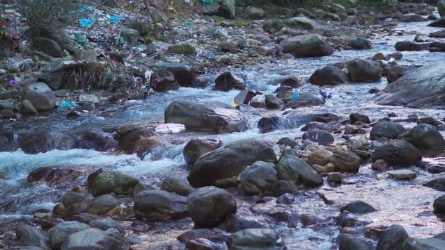 Closeup shot of river Parvati flowing in between mountains at Kasol with plastic waste around the river with some plastic waste floating in the stream. Waste dumped on side of river in Himachal. 