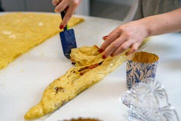 Woman using a spatula rolls the dough with raisins. Tools and ingredients are laid out on table. process of making buns.