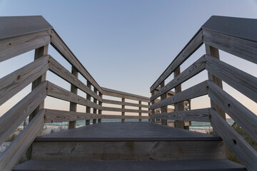 Wooden footbridge with railings turning to right above sand dunes on a beach at Destin, Florida. Walkway heading to the beach against the horizon skyline background.