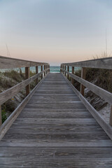 Vertical shot view of a wooden pathway with railings in between grassy sand dunes in Destin, Florida. Pathway heading to the beack with blue ocean under the horizon skyline.
