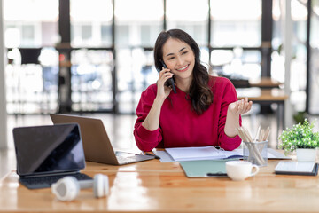 Corporate Communication. Asian Businesswoman Talking On Mobile Phone Working On Laptop In Modern Office. Free Space
