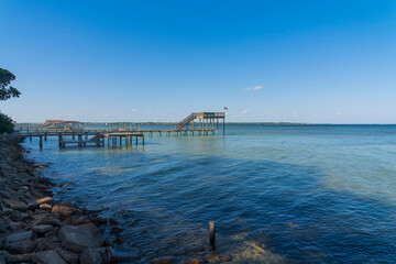 Obraz premium Wooden pier and dock at the bay in Navarre, Florida. Views from the shore with rocks of docks with view decks against the clear blue skyline background.