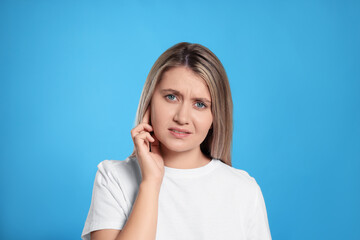 Young woman suffering from ear pain on light blue background