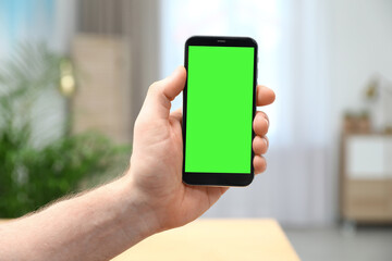 Man holding smartphone with green screen indoors, closeup. Gadget display with chroma key. Mockup for design