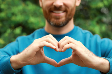 Happy man making heart with hands outdoors, closeup