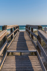 Wooden footbridge with step and railings heading to the beach at Destin, Florida. Footbridge over the sand dunes with notice sign on the right and views of ocean and skyline background.