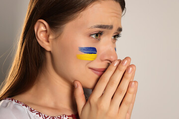 Obraz na płótnie Canvas Sad young Ukrainian woman with clasped hands on beige background, closeup