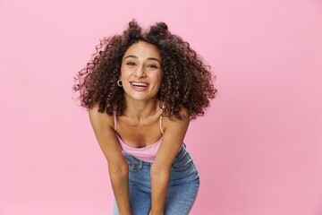 Obraz na płótnie Canvas Woman with curly afro hair model poses on a pink background in a pink T-shirt, free movement and dance, look into the camera, smile with teeth and happiness, copy space