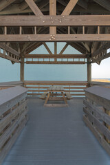 Wooden gazebo with dining table with seats near the building in Destin, Florida. Gazebo with wooden flooring against the sage green building wall at the background.