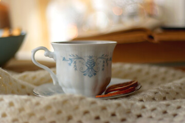 Vintage books, reading glasses, e-reader, cup of tea, bowl of biscuits and lit candle on the table. Selective focus.