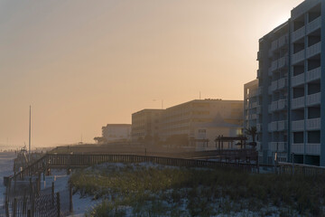 Sunset behind the row of the hotel buildings with grassy sand dunes at the front in Destin, Florida. There are wooden fences and sand dunes with footbridges connecting the beach and buildings.