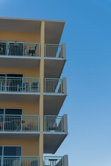 Fototapeta premium Balconies meeting at the corner of a hotel or apartment building in Destin, Florida. Vertical shot of building corner with yellow wall and white balcony railings against the clear blue sky.