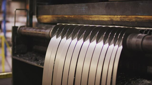 Tilt up shot of metal strips hanging on roll slitting machinery in factory