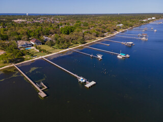 Aerial view of private docks with boat lifts at the front of a wealthy neighborhood in Navarre, FL. Villas with long pier on docks and tall trees on its yard.