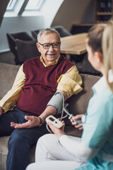 Home doctor is measuring blood pressure of old man at his home. Professional health support for...