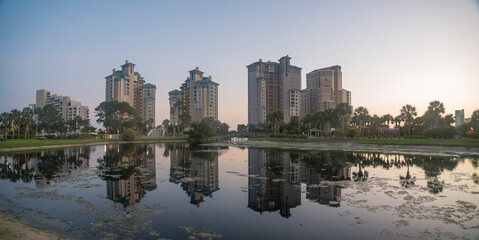 Fototapeta premium Panorama of decorative lake in a golf course with reflections of hotel buildings at Destin, Florida. Cityscape of hotels view from a golf course against the dusk sky.