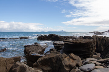 Fototapeta na wymiar Rocky coastline with blue sea and an island on background, Auckland, New Zealand.