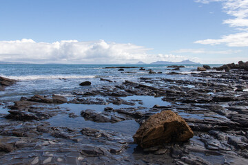 Rocky coastline with blue sea and an island on background, Auckland, New Zealand.