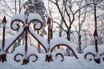 Close-up of a metal fence covered with snow against a sunset landscape