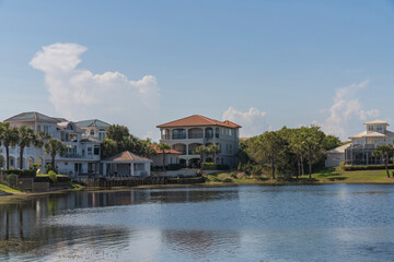 Obraz premium Mansions and villas with views of Four Prong Lake waterfront in Destin, Florida. There is a reflective lakefront views of the large residences against the pastel clouds in the sky background.