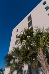 Low angle view of a multi-storey apartment or hotel with balconies in Destin, Florida. There are palm trees at the front of balconies of a building against blue sky.
