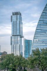 View of a condominium tower with tiered structure from Butler Metro Park in Austin, Texas. There are trees below the three buildings with curved structure on the right near the other two buildings.