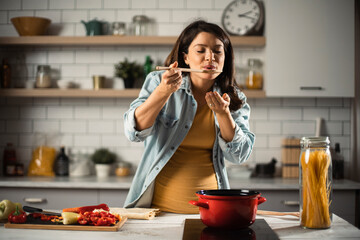 Beautiful pregnant woman preparing delicious food. Smiling woman having fun while cooking at home