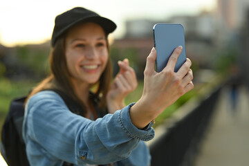 Cheerful female travel blogger recording video vlog with smart phone while standing on bridge with scenery view of river in Thailand