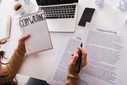 Cropped view of copywriter holding marker and notebook near devices at home.