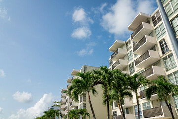 Views of foxtail palm trees at the front of apartment buildings at Miami, Florida. Modern residential building exterior with balconies under the sky above.