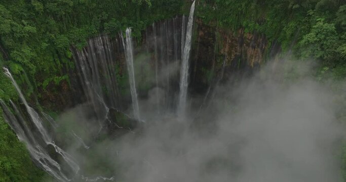 Aerial Shot Of Scenic Famous Cascade Flowing On Rock Formations, Drone Flying Forward Over Cloud - Java, Indonesia