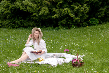 A smiling girl with a book on a blanket in the forest.