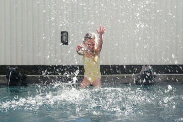 Portrait of adorable 5 years old girl sitting at the edge of swimming pool and splashing water with hands
