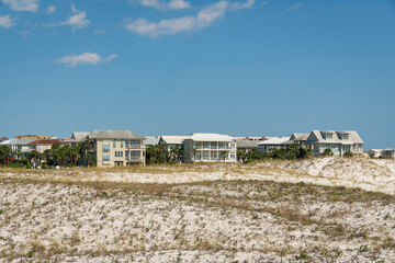 White sand dunes at the front of a residential area in Destin, Florida. There are views of large residential buildings against the sky background.