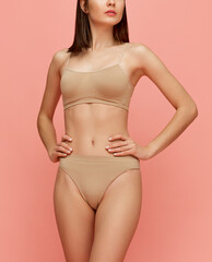 Fototapeta premium Body positivity. Cropped image of slim healthy female body posing in comfortable beige underwear over pink studio background. Concept of body and skin care, fitness, natural beauty, health, wellness.
