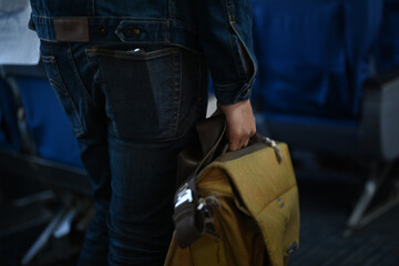 Cropped image of man passenger with bag walking the aisle on plane. Travel, transportation,...