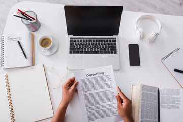 Top view of man holding papers with copywriting lettering near notebooks and devices at home.
