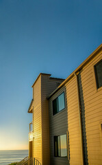Obraz premium House exterior against sea and sky at sunset in Del Mar Southern California. Facade of a beach home with sunlit walls and view of the calm beach and golden horizon.