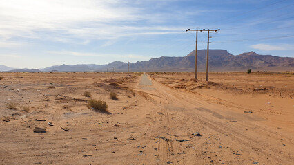 Long, straight and quiet road tracks in Middle East desert landscape with mountainous backdrop in Jordan