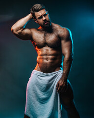 Obraz na płótnie Canvas Big muscled man in white towel. Handsome hunk posing is studio. Naked male model with muscles and hairy body at dark background. Bodybuilder wearing only bath towel. Sexy athlete with six pack abs.