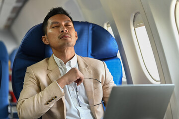 Millennial businessman distracted from computer work while sitting comfortable seat in airplane cabin
