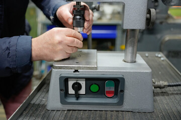 A man's hands setting up a drilling machine. The drilling machine details in focus. Rough male hands