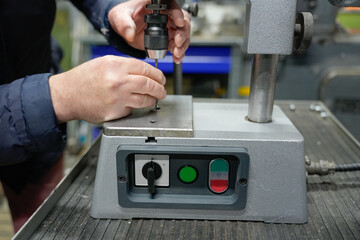 A man's hands setting up a drilling machine. The drilling machine details in focus. Rough male hands
