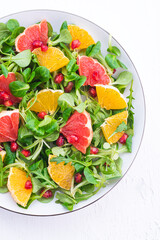 Spring citrus salad with oranges, grapefruit, pomegranate seeds and arugula. Sweet-salty flavors. Bright, delicious recipe full of vitamins, healthy food, white background. Plant based diet
