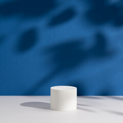 Empty white round podium and shadows on dark blue background. Showcase for product presentation. Pedestal for beauty cosmetic advertising. Minimal still life. Front view. Square photo.