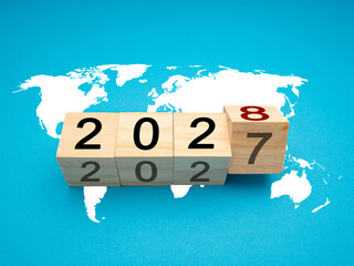 Wooden cubes with the letters 2027 change to 2028 over the world map on blue background