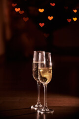 Two glasses of champagne, which stand on a black background with a beautiful bokeh, glasses against the background of hearts, the concept of Valentine's day, romantic dinner. Copy space. High quality