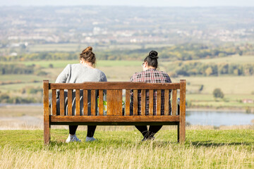 Salisbury Wiltshire, uk, 10, October, 2022 two friends sitting on wood bench over looking sailsbury plain